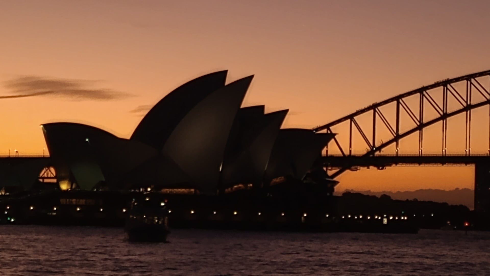 Silhueta da Ópera de Sydney e da Harbour Bridge contra o céu dourado do pôr do sol